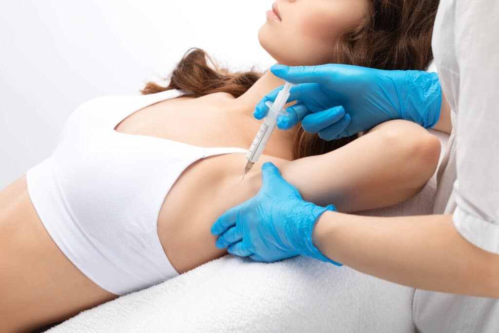 Doctor administering botulinum toxin injections in a woman's underarm area to treat hyperhidrosis in a cosmetic clinic