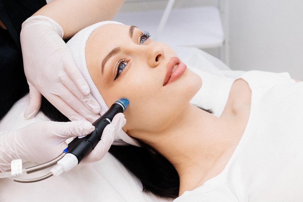 Cosmetologist performing a Hydrafacial on a woman's face in a beauty clinic to promote healthy, glowing skin.