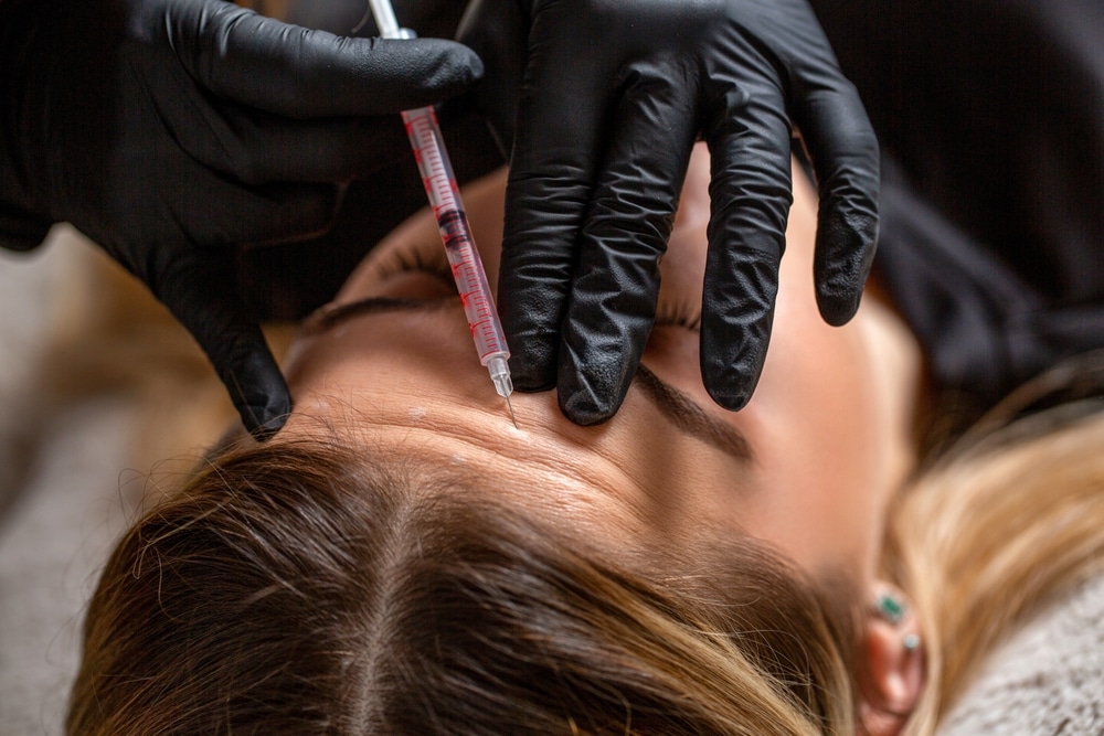 Young woman receiving Botox forehead injection for anti-aging treatment from cosmetic specialist.