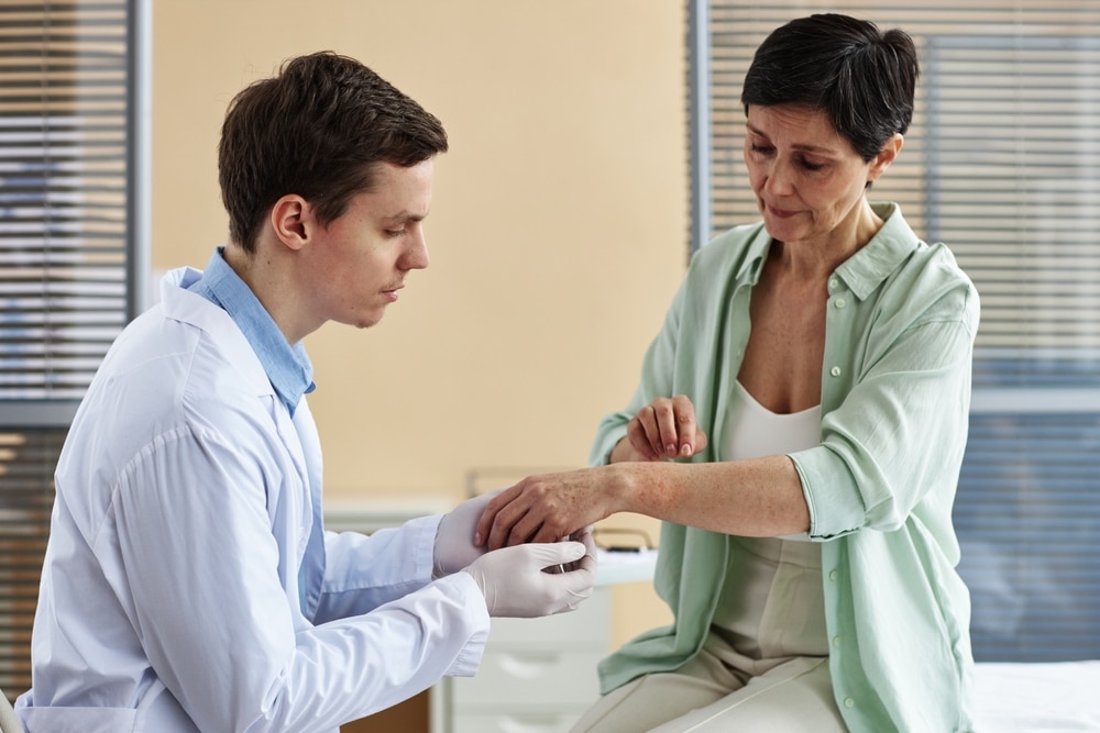Side view of doctor examining mature woman’s hands during consultation in dermatology clinic.