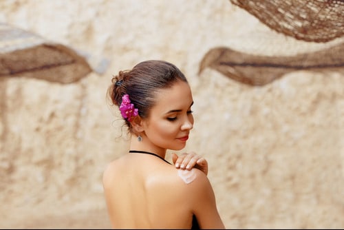 Woman on beach checks her exposed shoulder for sun damage.